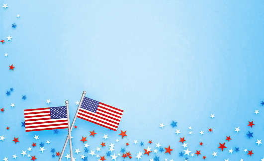 Tiny American flag pair sitting amid star shaped confetti on blue background. Horizontal composition with copy space. Directly above. 4th of July Independence Day concept.