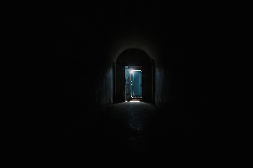 Dark tunnel and the door  silhouette with a light behind it at the end.