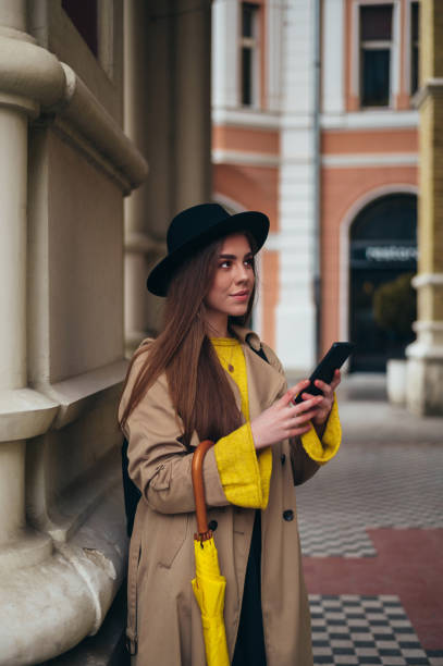 istock Young beautiful woman using a smartphone and holding a yellow umbrella 1317007194