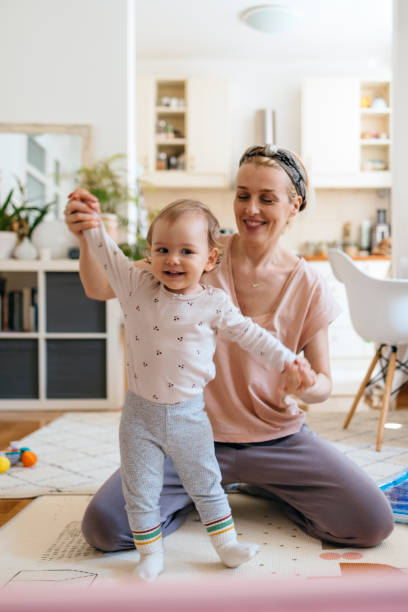 Mother holding hands of baby girl while dancing Beautiful young woman playing with cute daughter in living room. Smiling mother is holding hands of baby girl while dancing. They are enjoying in living room at home. babyhood stock pictures, royalty-free photos & images