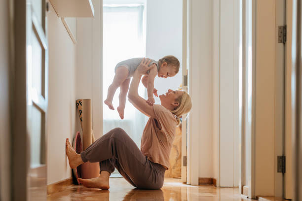 playful mother and baby daughter at home - baby carrier fotos imagens e fotografias de stock