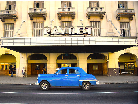 Havana, Cuba 2016- Vintage blue car driving in front of historic Payret movie theater (Teatro Payret) completed in 1951 with seating for 1890 people. The theater is located in the Habana Vieja area of central Havana, 3 minutes from the capital building overlooking Central Park.
