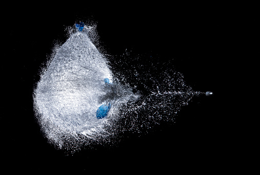 explosion of a water filled balloon on a black background, shot through by a bullet, high speed photography, refreshing explosion, frozen gun shot, horizontal