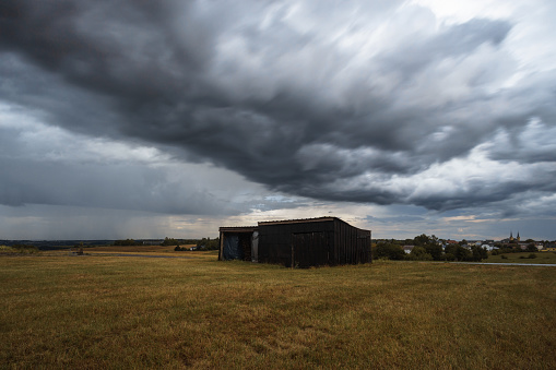 clouds over lone barn on dry meadow during thunderstorm and rain in summer