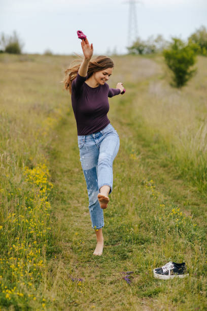 Barefoot young woman with stockings in her hands having fun in beautiful green field