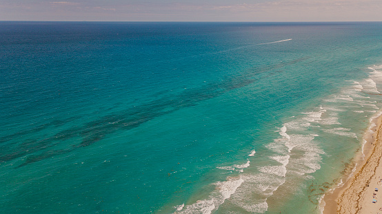 Aerial Overview of a Vibrant Teal Ocean Seashore Filled with Colorful Beach Umbrellas on Palm Beach, Florida at Mid-Day During COVID-19 in May of 2021.
