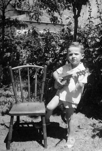 Image taken in the early sixties, Little boy playing guitar at his backyard