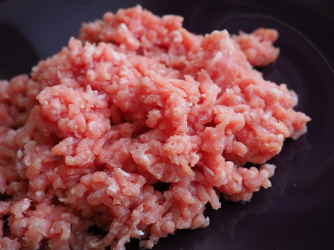 Minced meat on a purple ceramic large plate. Delicious fresh ground meat for making cutlets, steaks, hamburgers, meatballs. Pork semi-finished products.