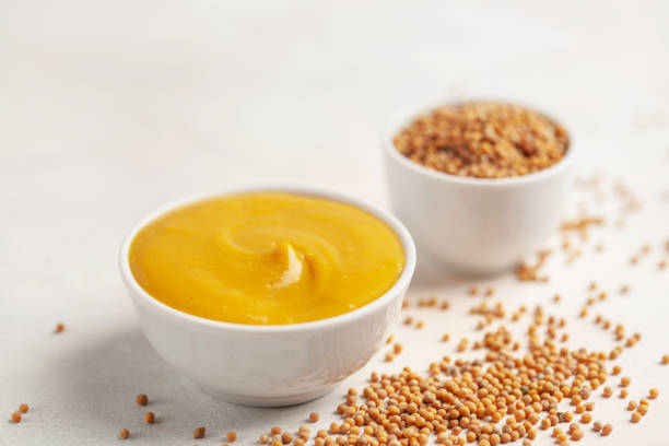 istock Mustard sauce in a bowl and seeds on a bright background. 1317042393