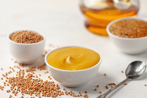 Mustard sauce in a bowl and seeds on a bright background.