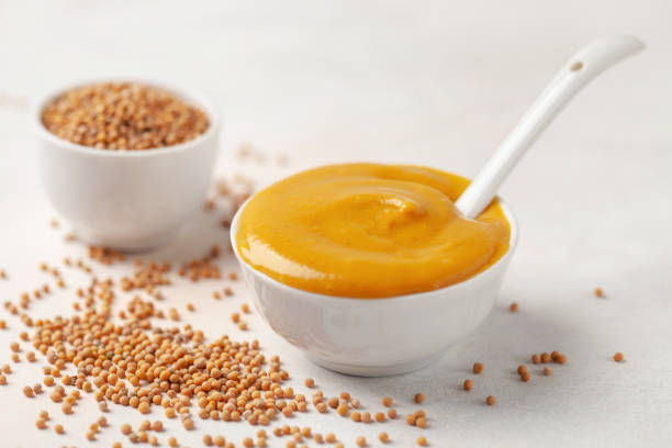 istock Mustard sauce in a bowl and seeds on a bright background. 1317042400
