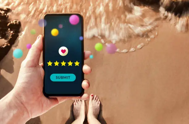 Photo of Customer Experiences Concept. Happy Client Using Smartphone to Giving Excellent Review for Online Satisfaction Surveys. Using Mobile Phone to Submit Positive Feedback. standing on Summer Sand Beach