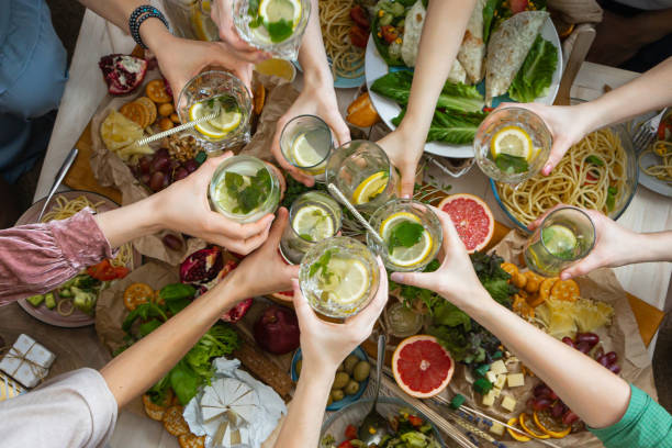 Top view closeup female friends hands cheers toasting glass of healthy beverage over serving table Top view closeup female friends hands cheers toasting with glass of healthy beverage over serving table. Woman arms celebrating hen-party birthday holiday meeting together enjoying food and drink bachelorette party stock pictures, royalty-free photos & images