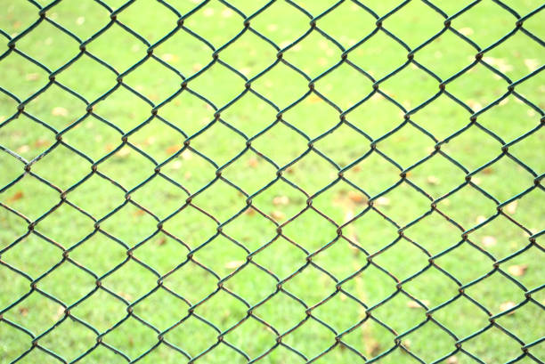 istock Old chain link pattern abstract fence with green grass field background. Focus foreground with soft, blurry background. Any backdrop, private property, prison, entrance, sports or game field concept. 1317059994