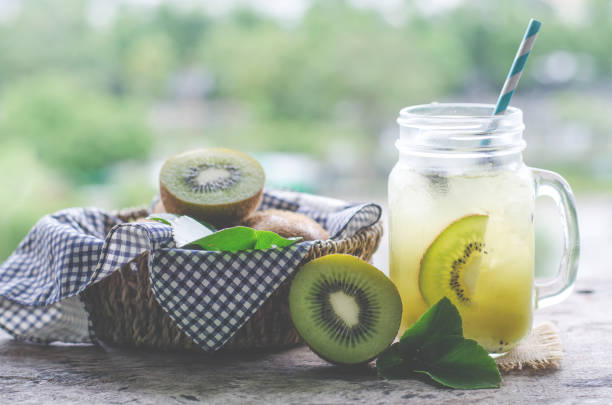 Fresh kiwi fruit juice in glass mug with some slice fruit over blur nature background in soft light tone