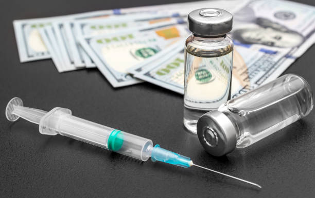 istock Vaccine vials with syringe and dollar bills on black. Close up. 1317062789