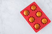 Red silicone baking dish with vegan carrot muffins over white marble background. Top view, copy space.