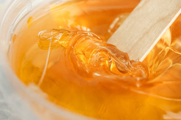 Sugar paste or wax honey in a transparent jar on a white background. Sugaring. Depilation and beauty concept. Waxing. Close-up.