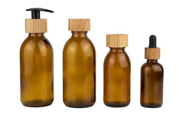 Set of assorted brown glass bottles with wooden lids for cosmetics. Dispenser with a straw and a pipette. Eco concept. Bottle for lotion, cream isolated on white background. Wooden cork. Zero waste.