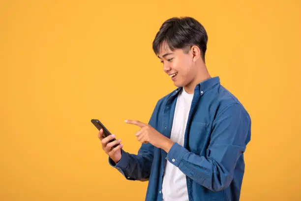 Photo of Image Asian man standing on orange background Using a mobile phone.