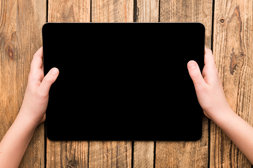 Hands hold digital tablet computer on wooden table