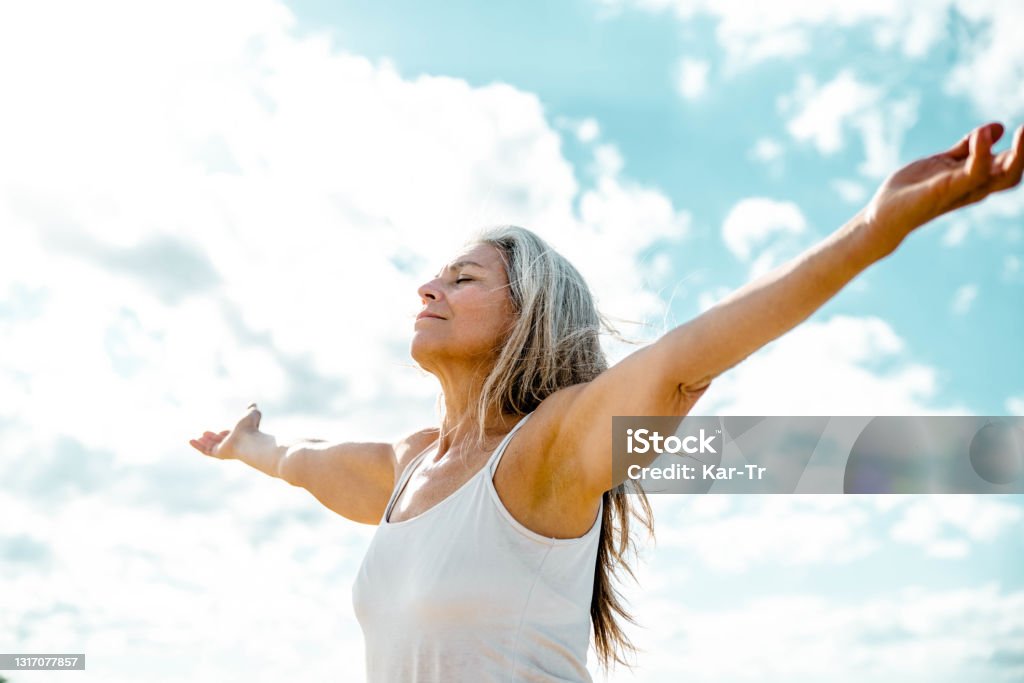 Joyful senior woman enjoying freedom standing with open arms and a happy smile looking up towards the sky - People and happiness concept Senior Adult Stock Photo