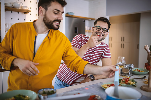 Photo of male friends standing around the kitchen island, having fun and preparing food together.