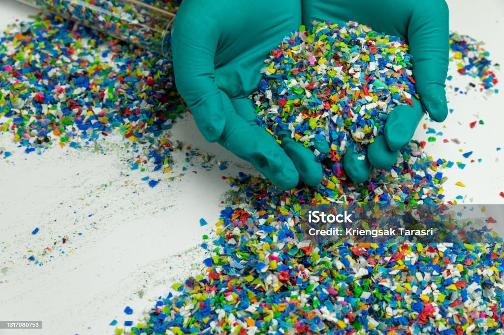 Crushed plastic on green gloved hand. Reuse of plastic. polymer beads. Scraps obtained from plastic waste. The world's plastic reduction policy. Scraps plastic on white background. Plastic Stock Photo