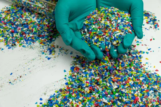 Photo of Crushed plastic on green gloved hand. Reuse of plastic. polymer beads. Scraps obtained from plastic waste. The world's plastic reduction policy. Scraps plastic on white background.