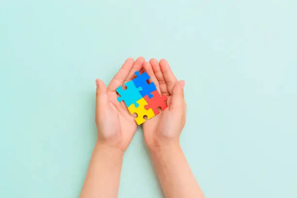 Photo of World autism awareness day. Hands of small child holding colorful puzzles. Concept - Autistic Pride Day. ASD. Banner. Top view. Layout