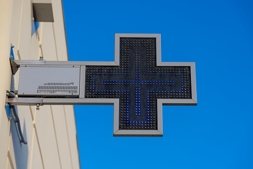 A blue pharmacy cross with LED lighting screwed to a house wall, where the cross is represented by LEDs.