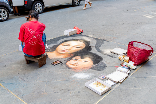 Florence, Toscana/Italy - 24.08.2020: A street painter painting a picture on the sidewalk showing a woman and a child