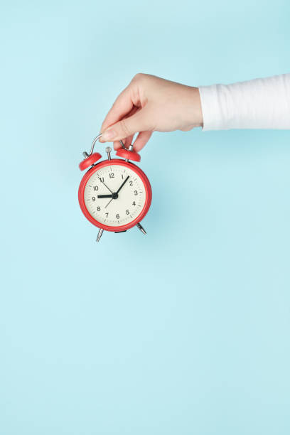 istock Red alarm clock in woman's hand on a blue background 1317086182