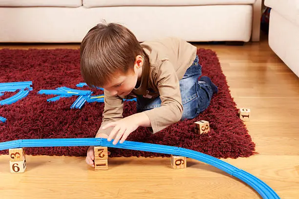 Little boy is building toy railroad using bricks