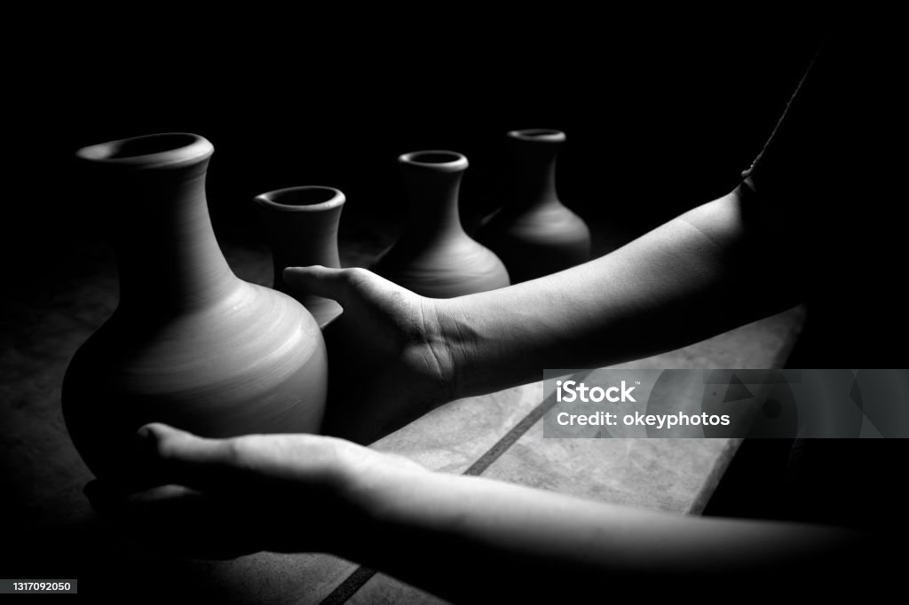 Man laying out his newly made pottery jugs A man is laying out his newly made pottery jugs with his hands. It is not clear who it is because the lower part of his body is visible. There are five pottery jugs in the photo. Black And White Stock Photo