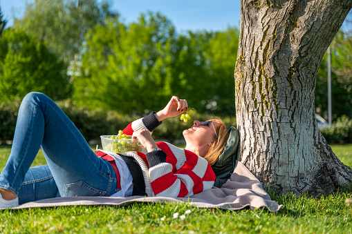 Adult woman in a public park reading a book and having a healthy lunch.