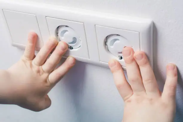 Photo of Two Child Hands Touching A Wall Socket With Safety Plugs - Prevent Child Hazard Concept