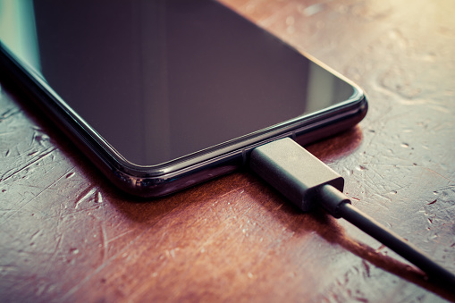 Black Smartphone With Connected Black USB Cable On Brown Wooden Table