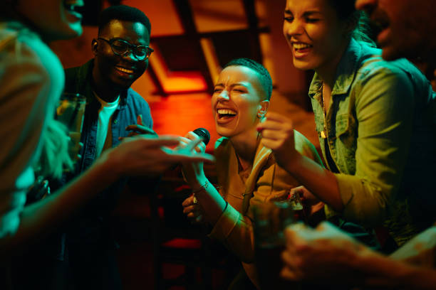 Group of happy friends singing karaoke during a night party at the pub. African American woman holding microphone and singing while partying with her friends at nightclub. karaoke photos stock pictures, royalty-free photos & images