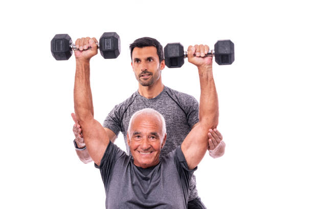 Elderly male client exercising with a fitness trainer, lifts dumbbells. On a white isolated background. stock photo