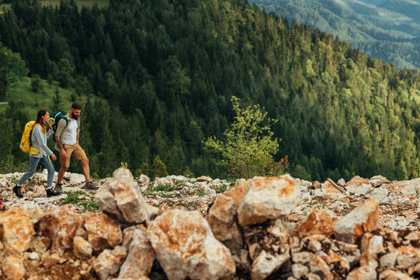 Rear view of a young hiker man in a yellow raincoat and a big backpack and outdoor sports eyewear standing on top of a rock hiking and walking in a fantastic mountain landscape on another side of Dolomiten mountains and a blue pond view of Drei Zinnen or Tre Cime di Lavaredo with a beautiful cloudy sky in South Tirol, Dolomites, Italia. Popular travel and hiking Destination in the world.