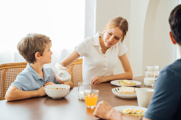 Girl pouring milk for boy during breakfast Smiling teenage caucasian sister pouring and serving milk for younger brother in bowl of cereals with handsome father watching during breakfast at home spanish breakfast stock pictures, royalty-free photos & images