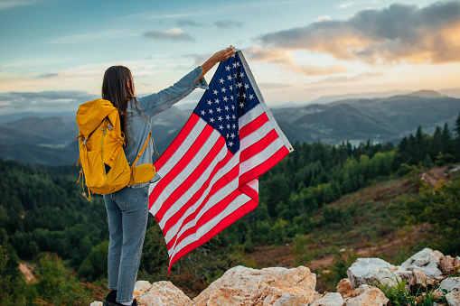 American flag - woman USA sport athlete winner cheering waving stars and stripes outdoor after in desert nature. Beautiful cheering happy young multicultural girl joyful and excited.