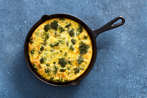 Oven baked omelet or quiche with broccoli, cheddar cheese on a blue background