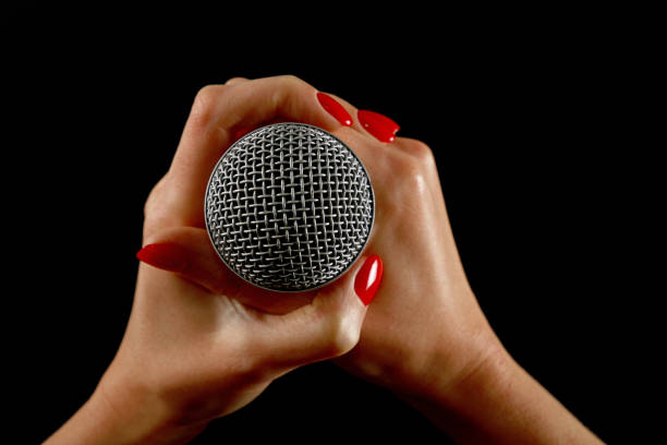 Woman hands with microphone isolated on black Woman holding microphone with two hands with red nails isolated on black background rocker nails stock pictures, royalty-free photos & images