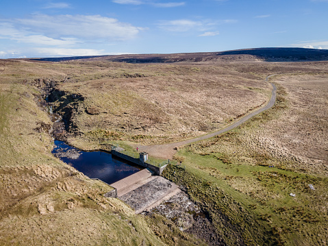 Aerial drone view of the river Inver and path to pumping station, County Antrim, Northern Ireland, where it passes through a small pumping station at Dungonnell, on a sunny summer day, with barren green landscape of the Antrim hills