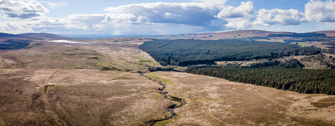 Aerial drone view of the green forestry landscape at Glenariff, County Antrim, Northern Ireland, on a sunny day with clouds in the sky and Dungonnell Reservoir in the distance, and the River Inver in the foreground