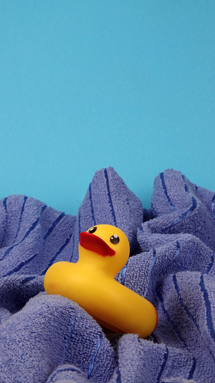 This is a yellow rubber duck toy on blue towel waves abstract concept photo of turbulent sea or ocean on blue copy space background.