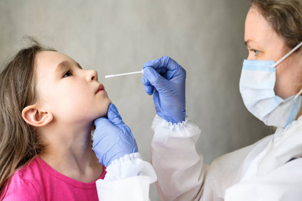 COVID-19 PCR test and kid, nurse holds swab for nasal sample from adorable child stock photo