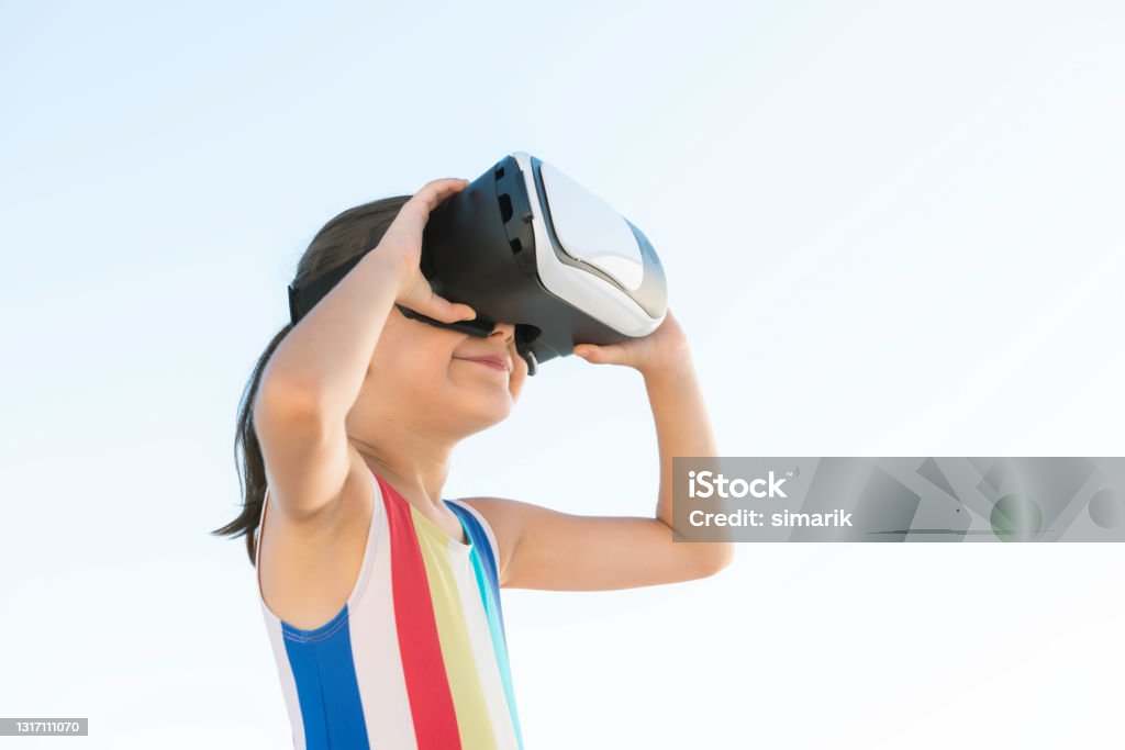 Fri Little girl wearing swimsuit is using Virtual Reality headset outdoors with a warm smile. She is playing a game. 360-Degree View Stock Photo